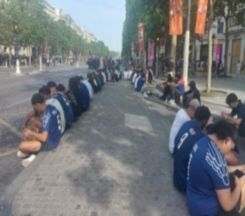 坐成一排，迟到的巴黎球迷用手机在香榭丽舍大道观赛